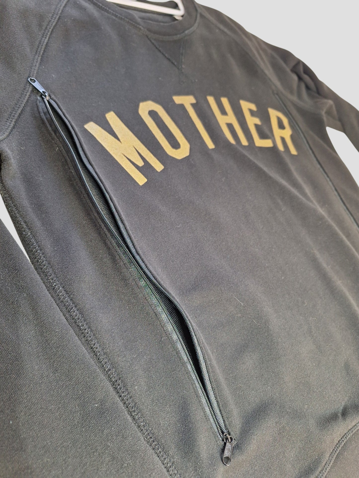 The Selfish Mother Upcycled Breastfeeding & Pumping Black/Gold MOTHER Sweatshirt (M) features bold yellow "MOTHER" lettering and a diagonal zippered pocket, offering stylish, sustainable nursing wear.