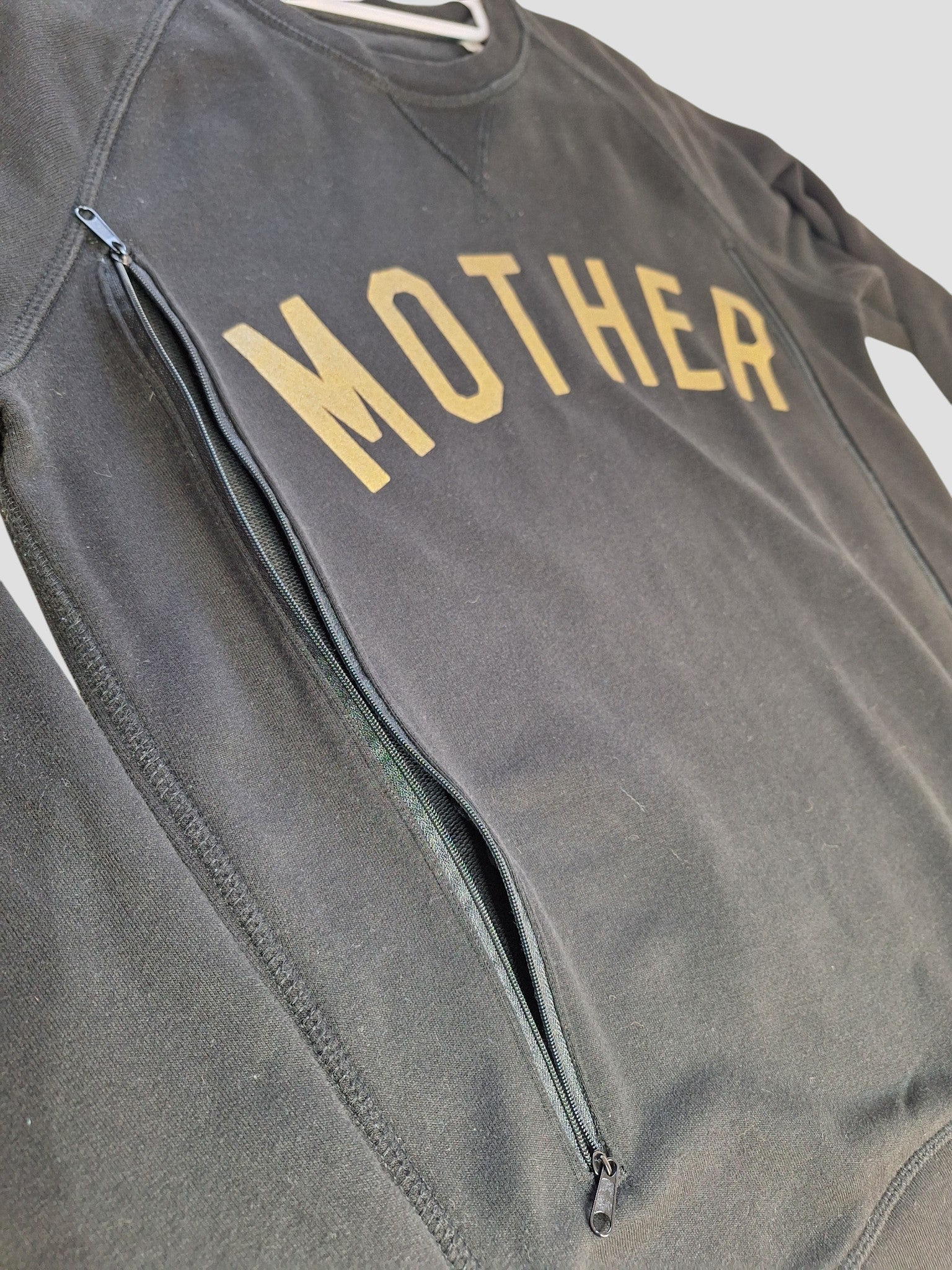 The Selfish Mother Upcycled Breastfeeding & Pumping Black/Gold MOTHER Sweatshirt (M) features bold yellow "MOTHER" lettering and a diagonal zippered pocket, offering stylish, sustainable nursing wear.