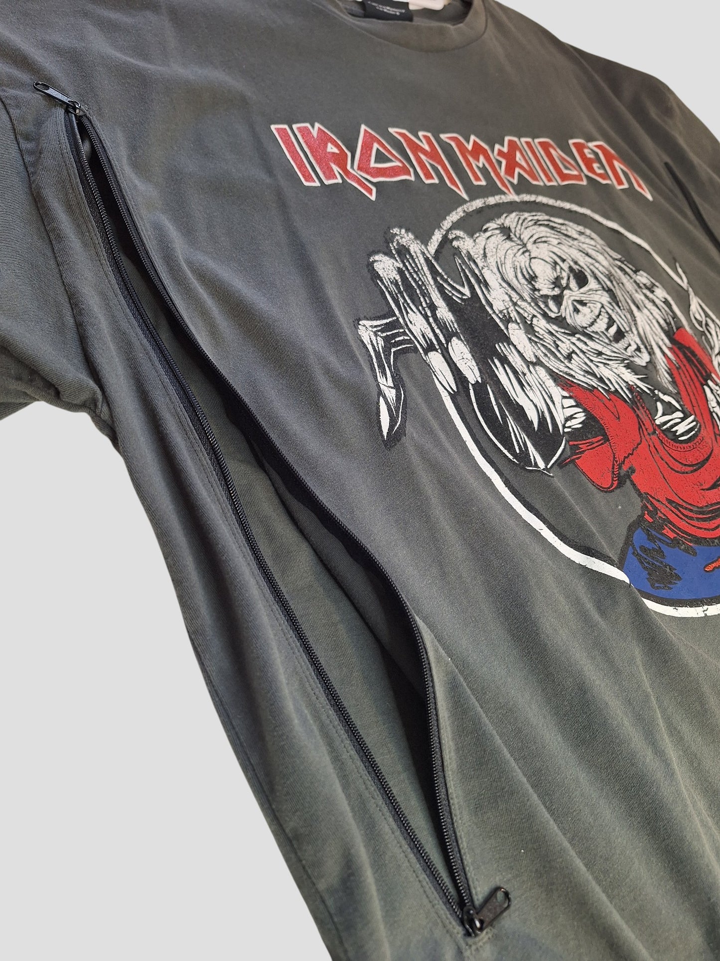 A close-up of a George Upcycled Breastfeeding & Pumping Grey/Red Glitter Iron Maiden Band T-shirt (UK18, 100400) shows a large side zipper—partially unzipped—with band art and logo visible on the front against a plain light gray background.