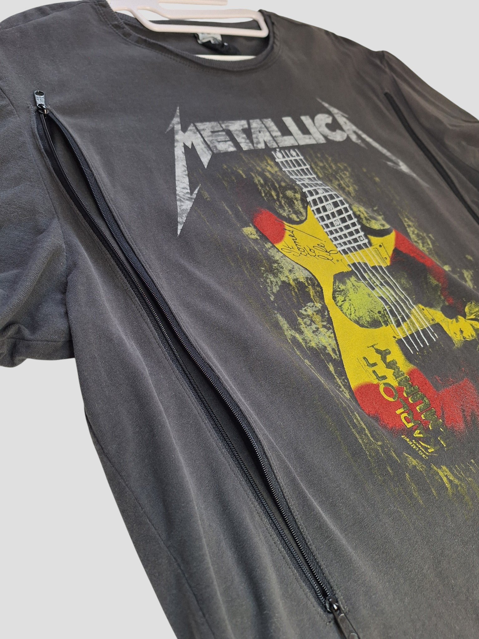 The Amplified Upcycled Breastfeeding & Pumping Metallica Guitar Band T-shirt XL (100353) features a colorful guitar graphic and diagonal zippers on preloved black fabric—eco-friendly, unique, and nursing-friendly. Shown laid flat on a light background.