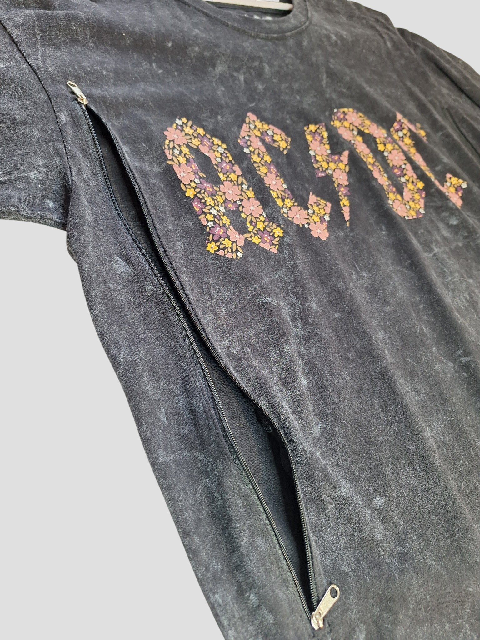 This upcycled AC/DC black band tee (L, 100387) features a floral logo and a diagonal zipper for easy nursing or pumping—an edgy, preloved choice for rock-loving moms.