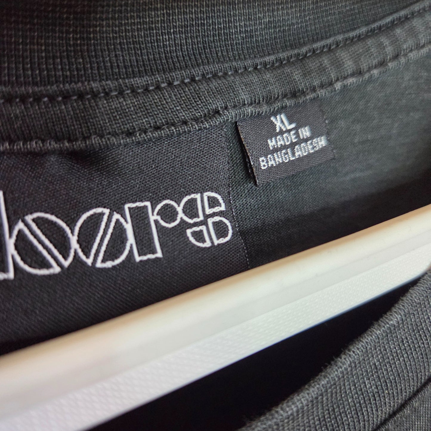 Close-up of a Primark Upcycled Breastfeeding & Pumping Black/Burgundy The Doors Band t-shirt (XL UK18/20, #100362) on a hanger, label reads MADE IN BANGLADESH—an eco-friendly wardrobe option.