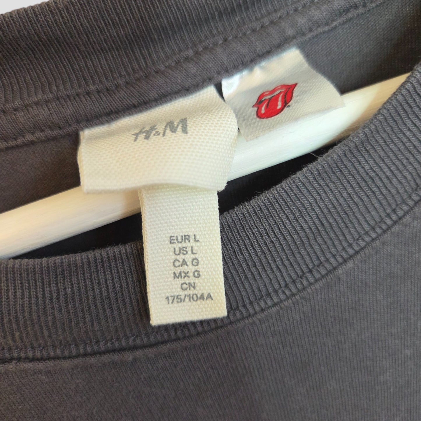 Close-up of a soft-touch H&M Upcycled Breastfeeding & Pumping Rolling Stones Band t-shirt (grey/red, white stars, size L) on a hanger, highlighting size and brand tags with the signature red tongue and lips graphic.