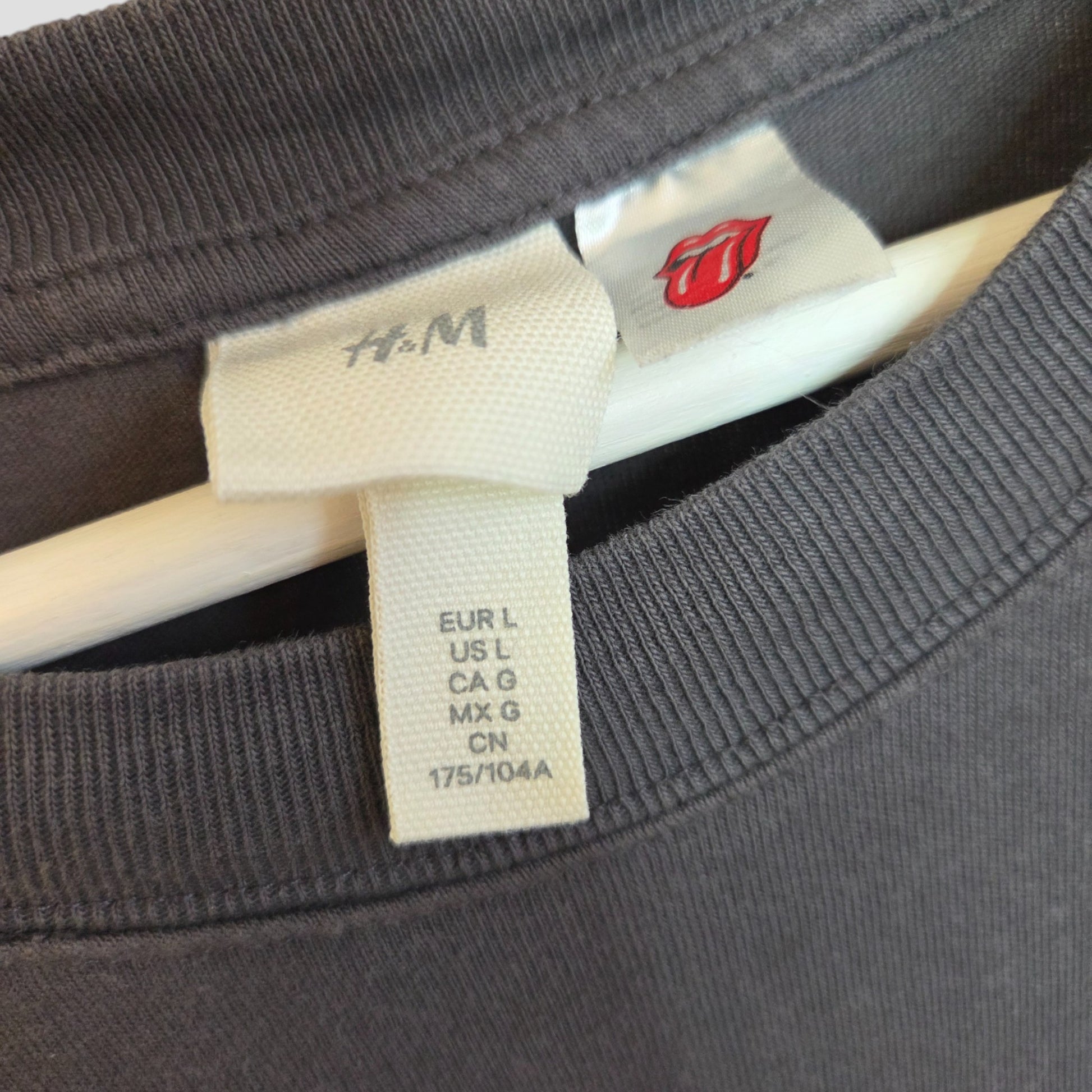 Close-up of a soft-touch H&M Upcycled Breastfeeding & Pumping Rolling Stones Band t-shirt (grey/red, white stars, size L) on a hanger, highlighting size and brand tags with the signature red tongue and lips graphic.