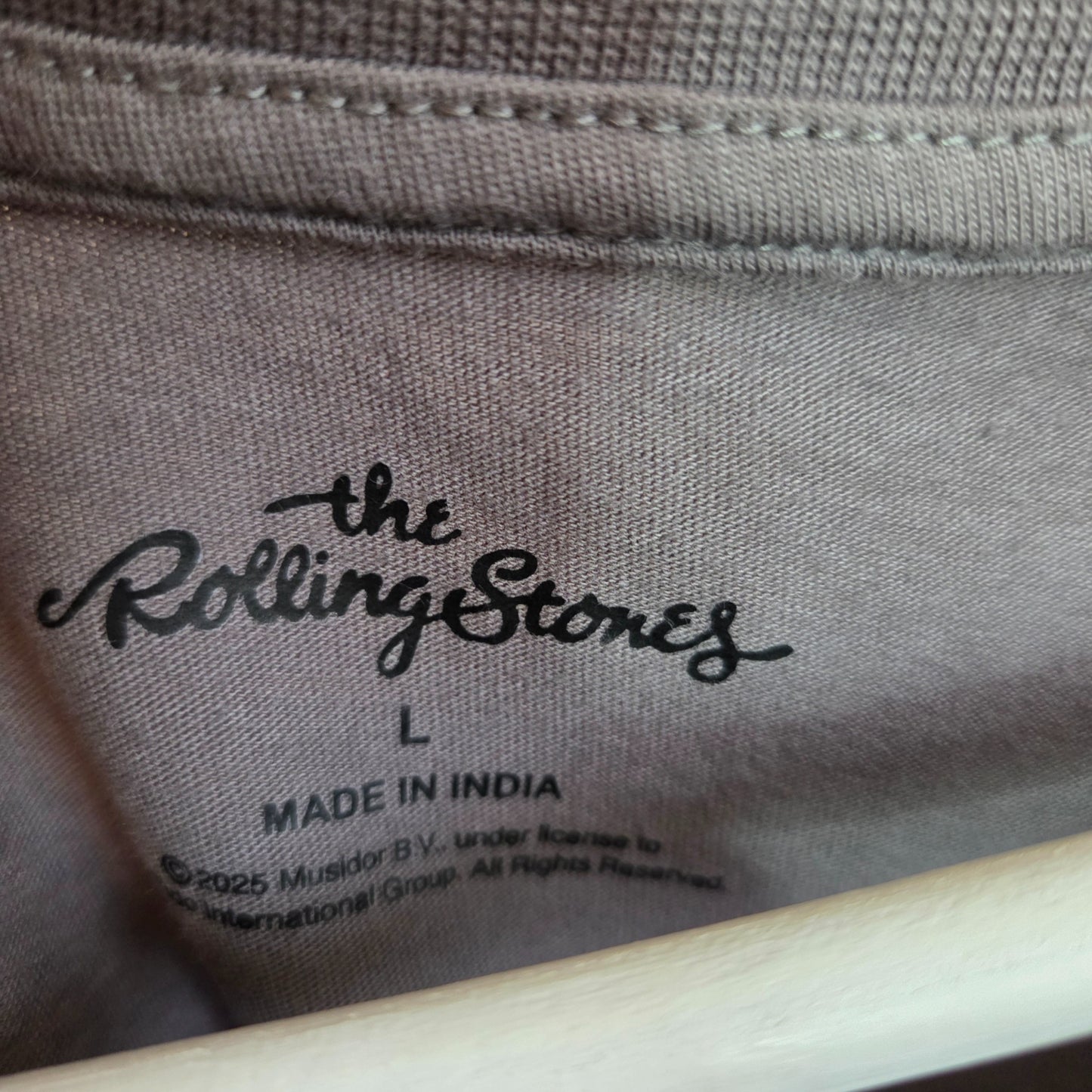 Close-up of a tag inside the upcycled breastfeeding & pumping grey/turquoise The Rolling Stones Band t-shirt (L), featuring The Rolling Stones logo, size L, and MADE IN INDIA—showcasing eco-friendly, stylish nursing wear.