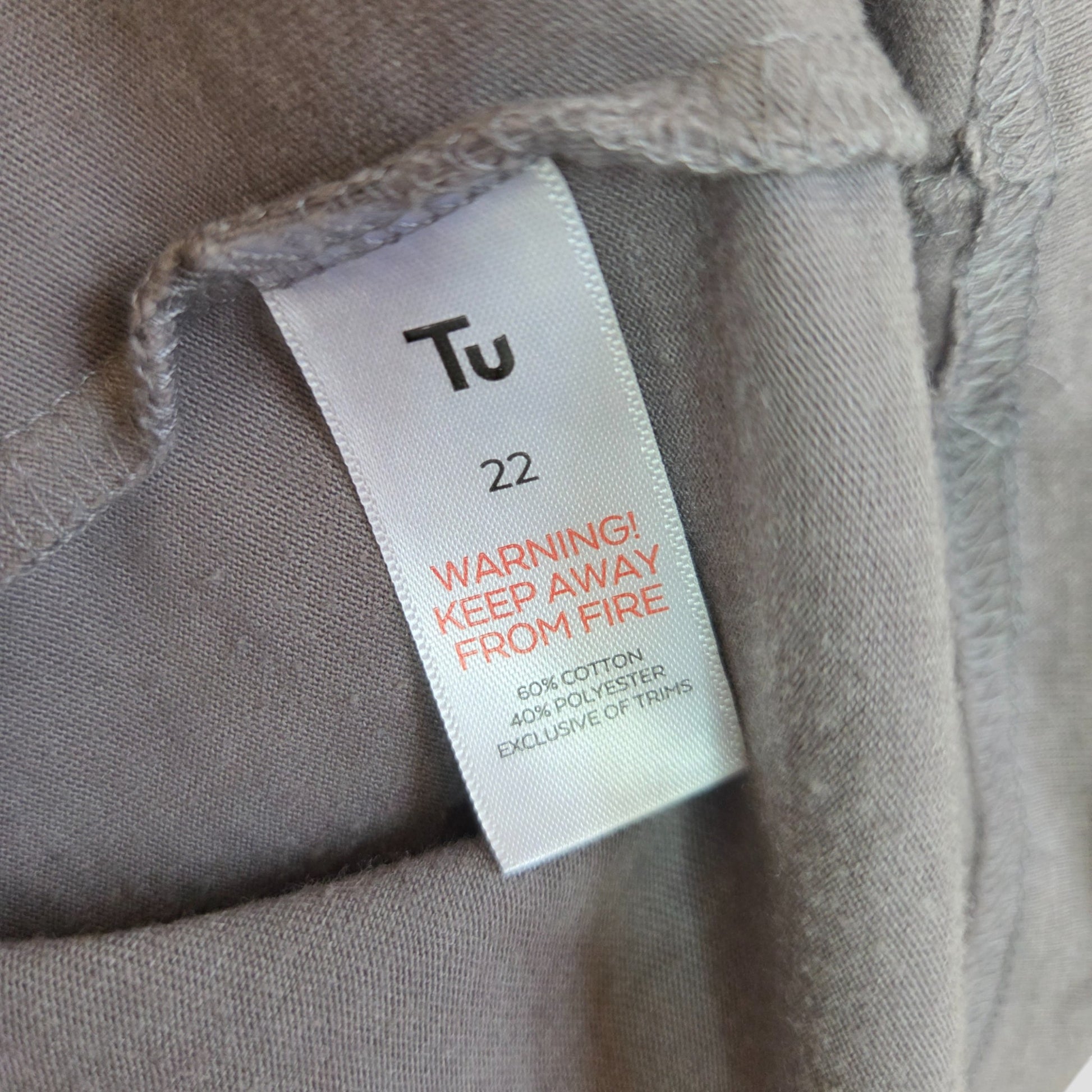 A close-up reveals the Tu label on an upcycled UK22 grey/pastel Bowie Band nursing t-shirt, with a red fire warning and material details (60% cotton, 40% polyester)—affordable fashion exclusive of trims.