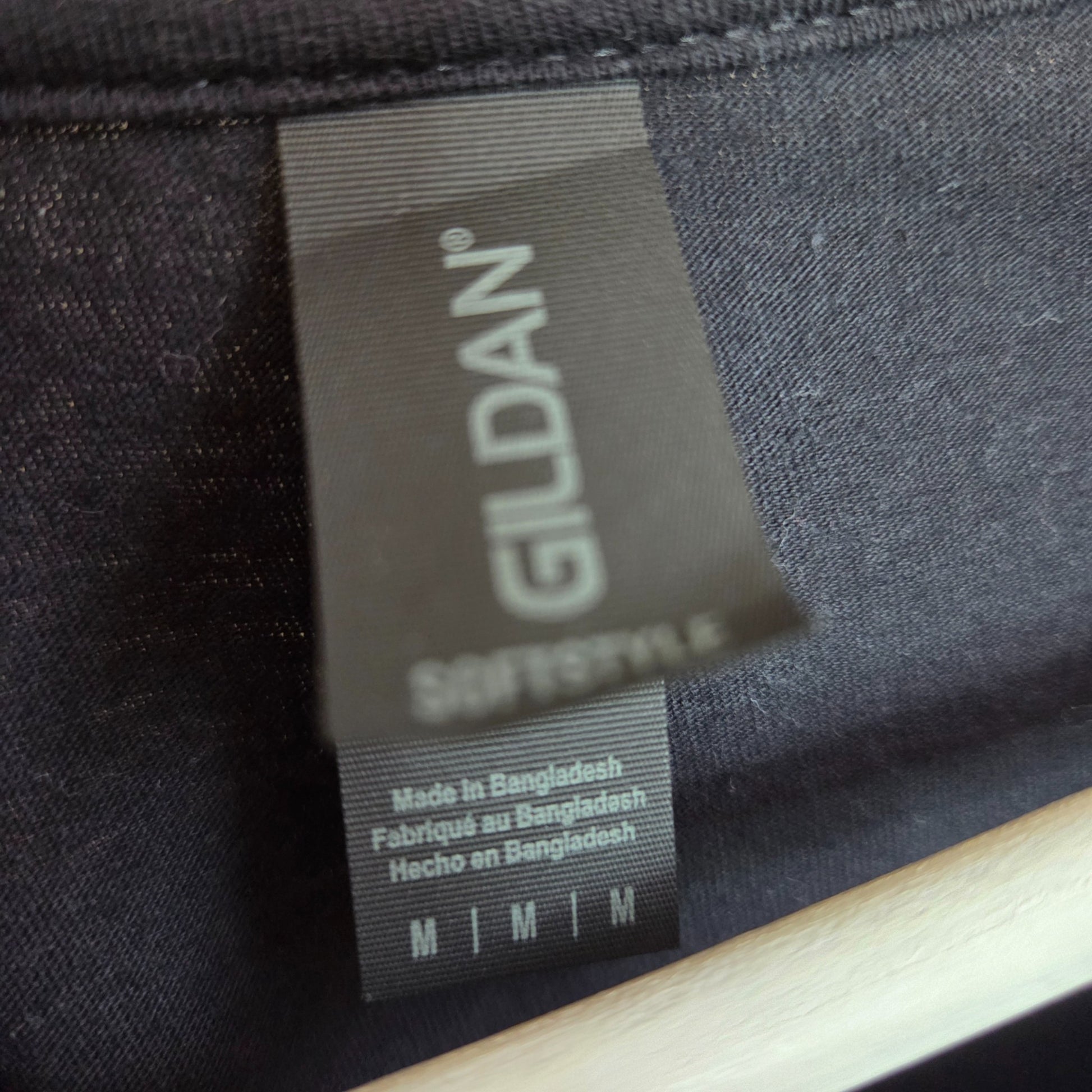 Close-up of a black Gildan tag marked M on the Upcycled Breastfeeding & Pumping Black/White Oasis Band t-shirt—ideal for eco-conscious nursing moms seeking unique, upcycled clothing. Made in Bangladesh.