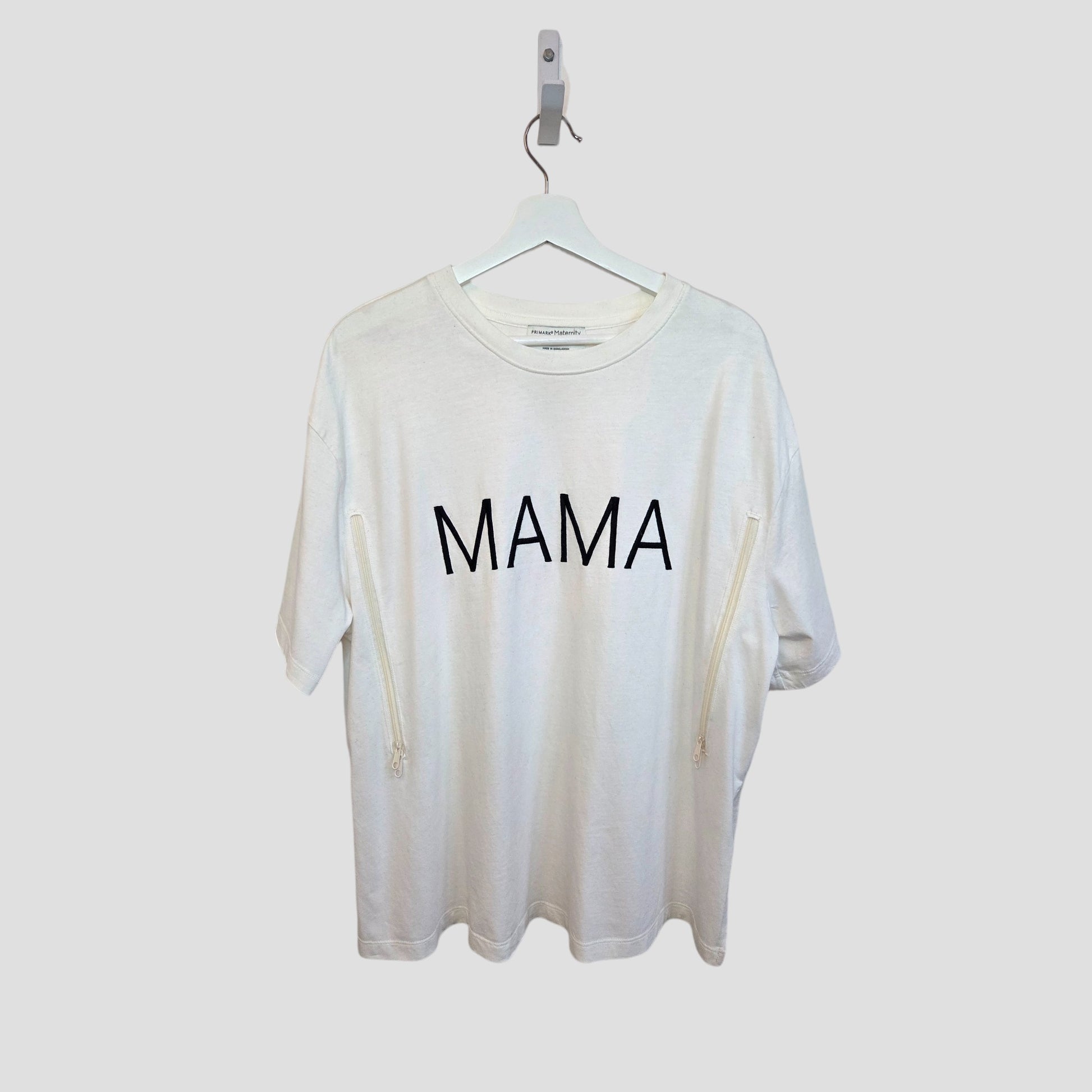 The Primark Upcycled Breastfeeding & Pumping White/Black MAMA t-shirt (M, 100373) hangs on a white hanger against a plain background, featuring bold black "MAMA" lettering on the front.