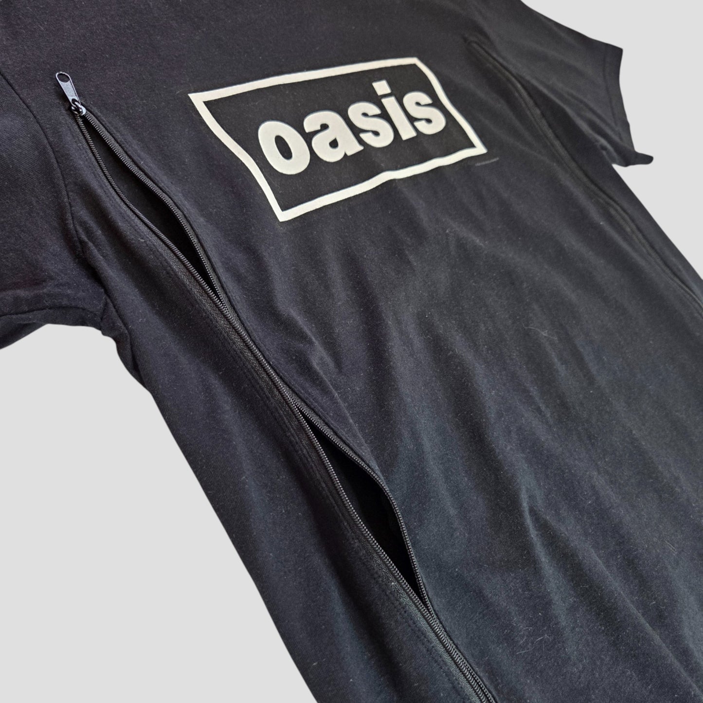 The Gildan Upcycled Breastfeeding & Pumping Black/White Oasis Band t-shirt (M, 100403) features a white oasis logo rectangle and a long front left vertical zipper, laid flat on a plain background.