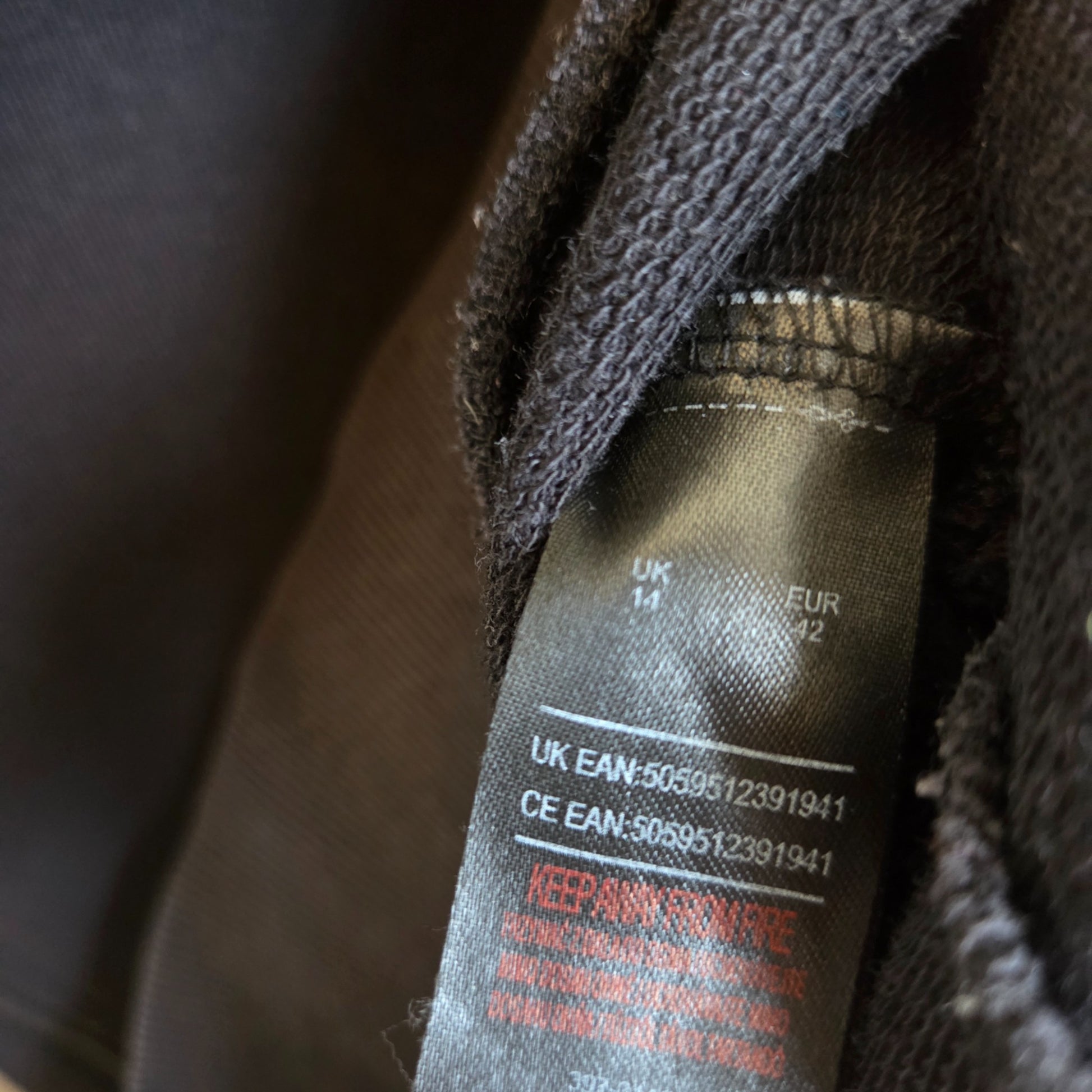 Close-up of a black clothing tag on an upcycled The Rolling Stones breastfeeding & pumping leopard band sweatshirt (UK14, EU42, 100411) with product codes and a red warning: KEEP AWAY FROM FIRE.