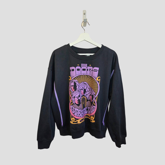 An upcycled H&M breastfeeding and pumping sweatshirt in black with purple accents hangs on a hanger. The front shows a colorful "The Doors Strange Days" graphic with illustrations in purple, yellow, and pink. Size L.