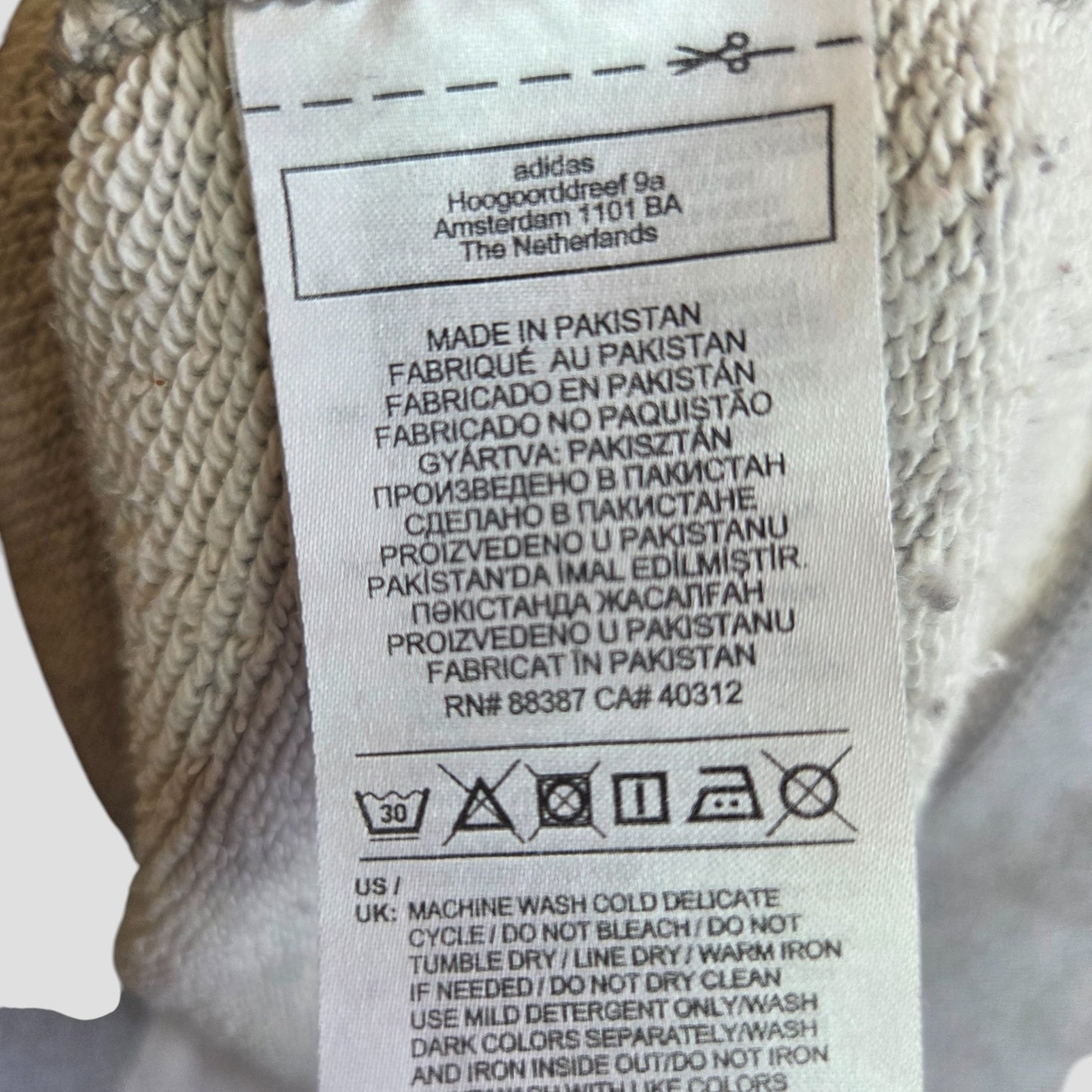 A preloved Adidas Upcycled Breastfeeding & Pumping Grey/White Logo Hoodie UK12 features a label with the Amsterdam address, multilingual washing instructions, care symbols, RN numbers, and notes it's made in Pakistan.