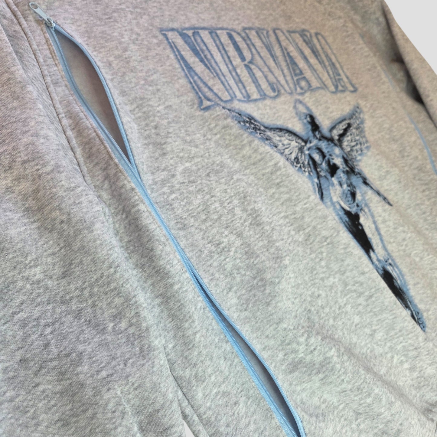 Close-up of an H&M Upcycled Breastfeeding & Pumping Nirvana Band Sweatshirt in light grey/blue, size L, with blue anatomical angel and "Nirvana" print on the front and a partially open zipper showing the light blue track.