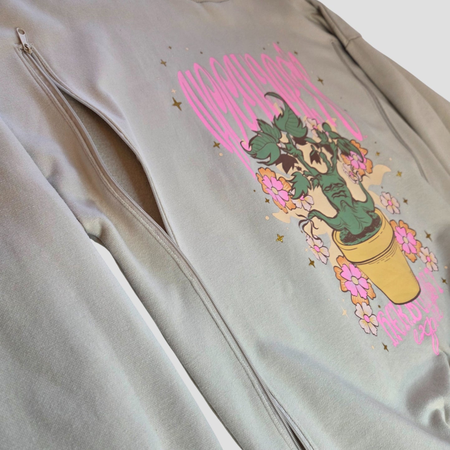 Upcycled beige Harry Potter breastfeeding sweatshirt by George (UK12/14), with side zipper for nursing and pumping. Features a colorful graphic of a potted plant, pink flowers, yellow stars, and bold "Monstera" text.