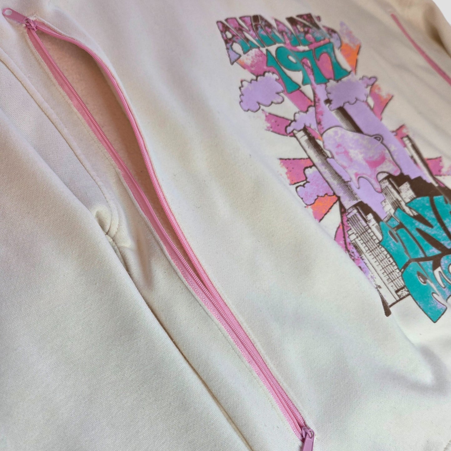 A close-up of an upcycled Primark Pink Floyd cream-colored sweatshirt, size L, featuring pink details and a colorful graphic—ideal for fans of preloved breastfeeding or nursing wear.