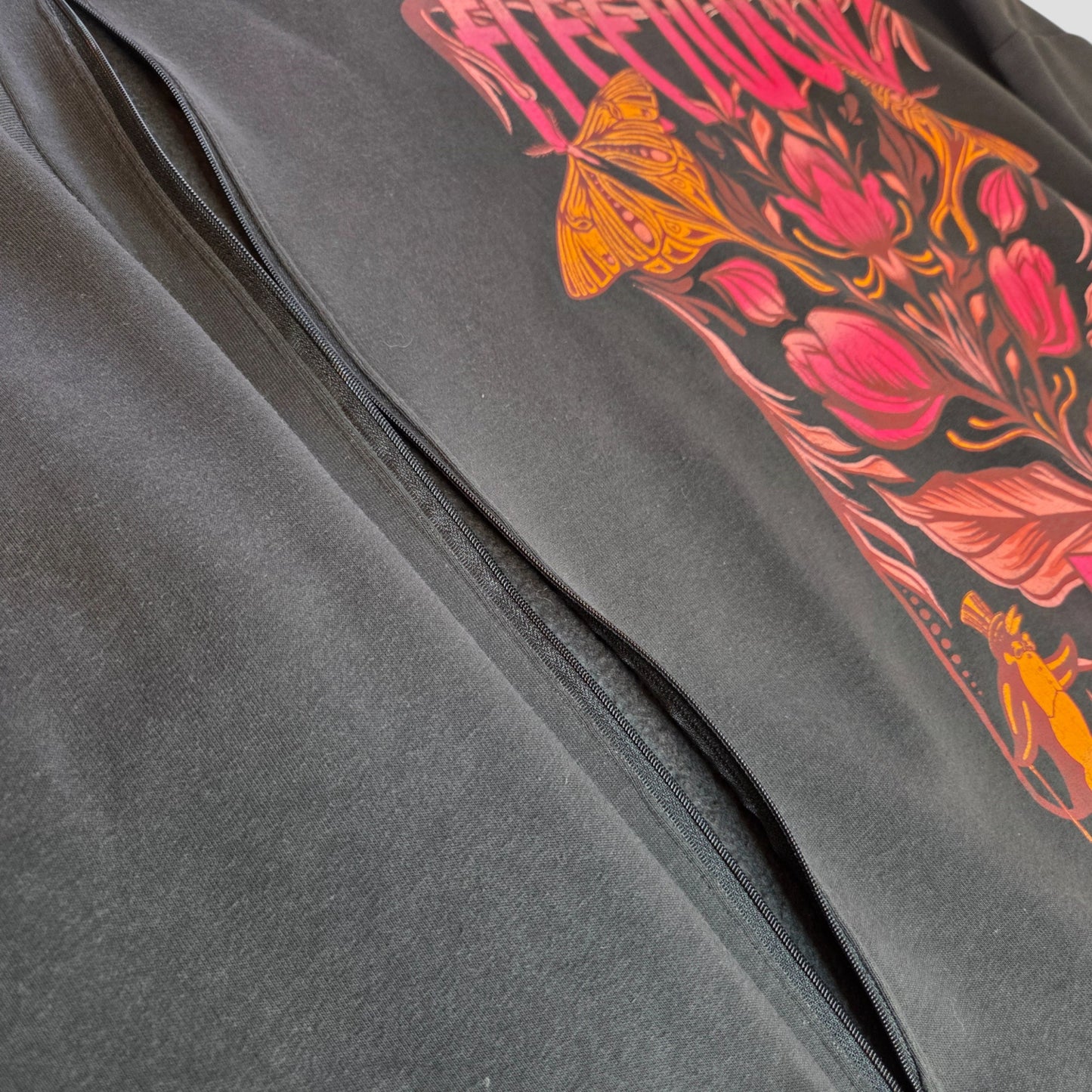 Close-up of an upcycled Primark breastfeeding & pumping floral Fleetwood Mac band sweatshirt (XL, UK18/20): black garment with a colorful floral graphic, featuring orange and pink butterflies and a visible central seam.