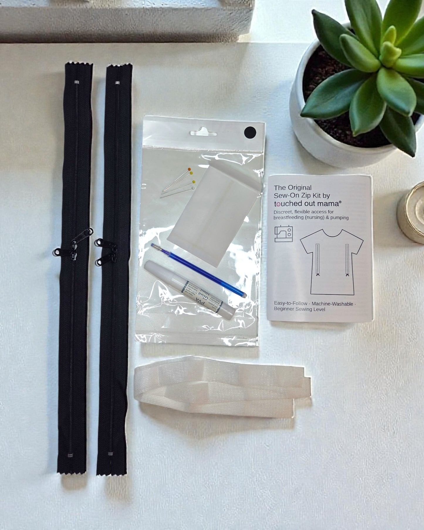 The Original Sew-On Zip Kit for Breastfeeding by touched out mama includes zippers, needles, thread, glue, pen, instructions, and a succulent—perfect for DIY repair or customizing your nursing top at home.