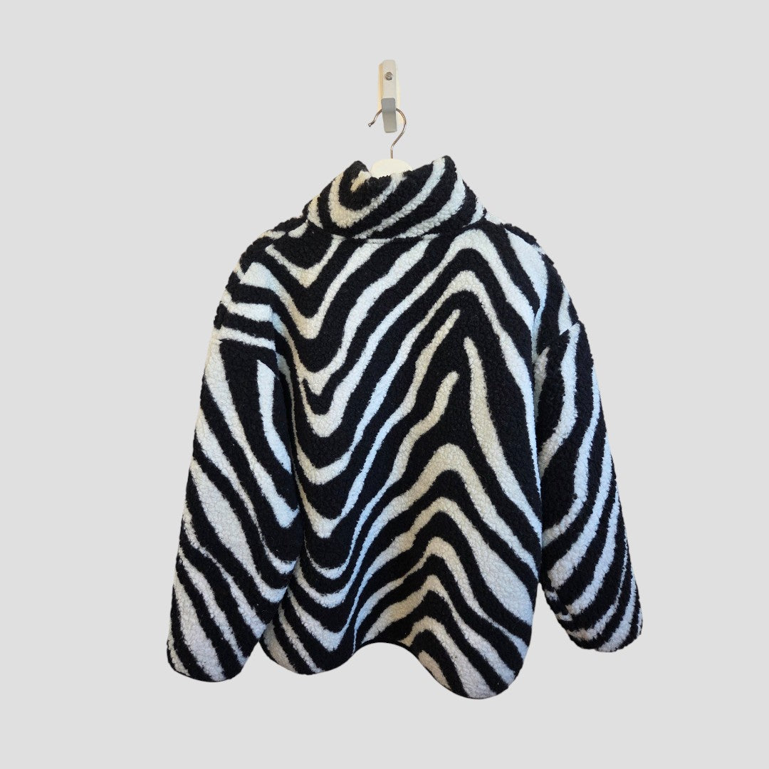 The Primark Upcycled Breastfeeding Zebra Zip Oversized Fleece (M, 100478)—a black and white high-collar jacket—hangs on a white hanger against a plain light gray background.