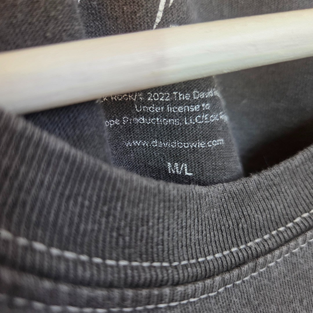 Close-up of the David Bowie Upcycled Breastfeeding & Pumping Saxophone Band t-shirt (M/L, 100458), with inner label showing "The David Bowie Archive, 2022," hanging on a white hanger. Visible collar stitching adds detail.