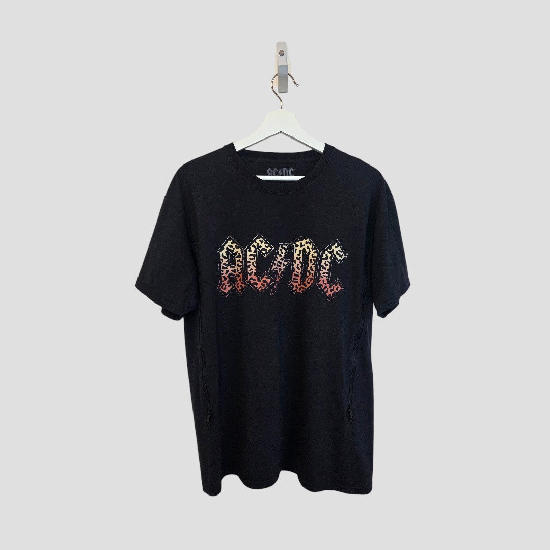 A black leopard AC/DC Upcycled Breastfeeding & Pumping Band T-shirt (L) by AC/DC hangs on a white hanger against a light gray background, featuring the band logo in a fiery red and yellow gradient design on the front.