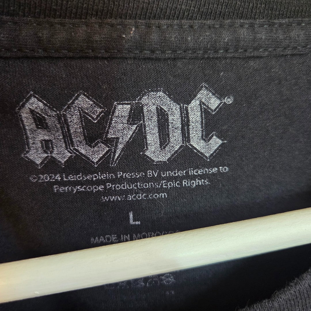 Close-up of the AC/DC Upcycled Breastfeeding & Pumping Black Leopard Band T-shirt (L), featuring a bold logo tag with licensing info—a stylish, eco-friendly choice for nursing fans.