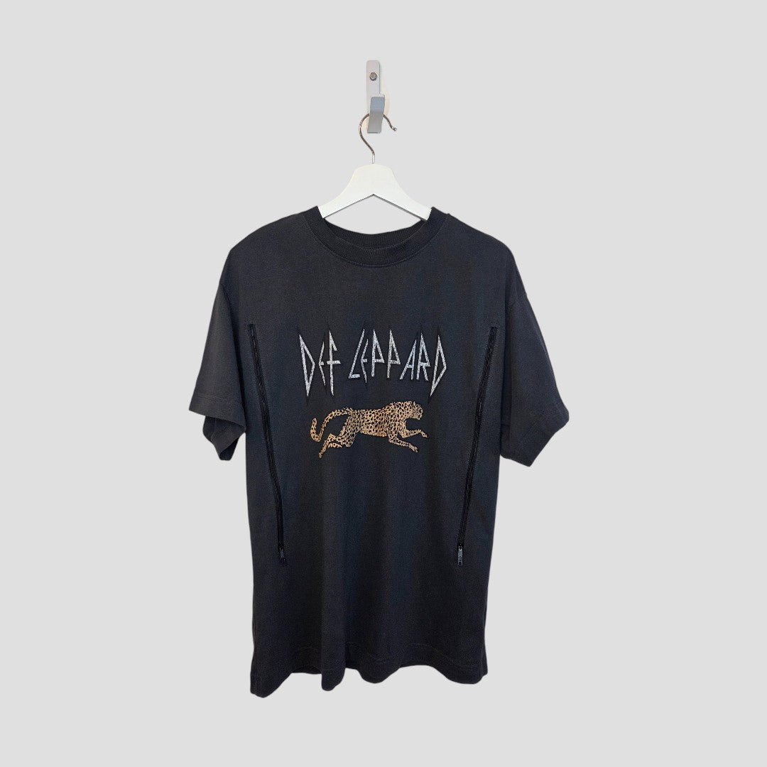 An upcycled grey Def Leppard leopard band T-shirt by H&M for breastfeeding and pumping (size S, 100474) hangs on a white hanger—an eco-friendly classic rock style set against a plain light gray background.