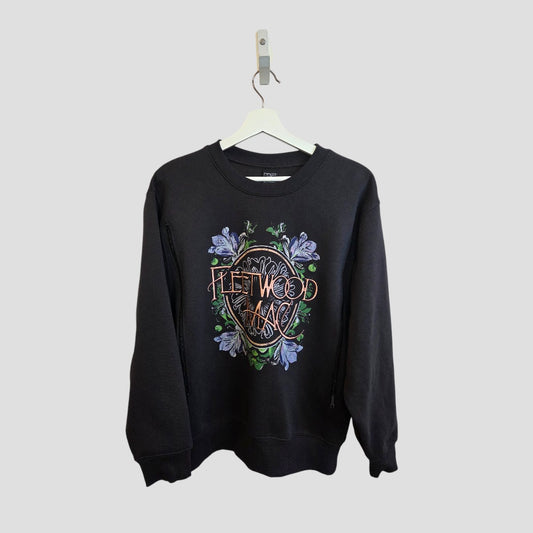 A black Primark crewneck sweatshirt (Upcycled Breastfeeding & Pumping Fleetwood Mac Band Sweatshirt S, 100433) with colorful graphics and floral embroidery, designed for nursing, hangs on a white hanger against a light gray background.