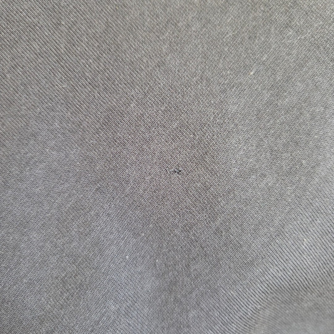 Close-up of a gray fabric with fine diagonal weave and a tiny, barely visible hole near the center from an Upcycled Breastfeeding & Pumping Black Metallica Skull Band t-shirt XS (100107) by H&M, designed as an eco-friendly affordable option.