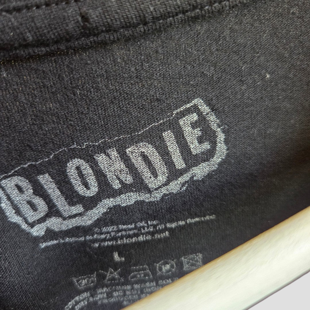 A close-up of a black fabric label reading BLONDIE in bold, distressed white letters, with company and website info below, featured on the affordable Upcycled Breastfeeding & Pumping Black Blondie Band t-shirt L by Blondie.