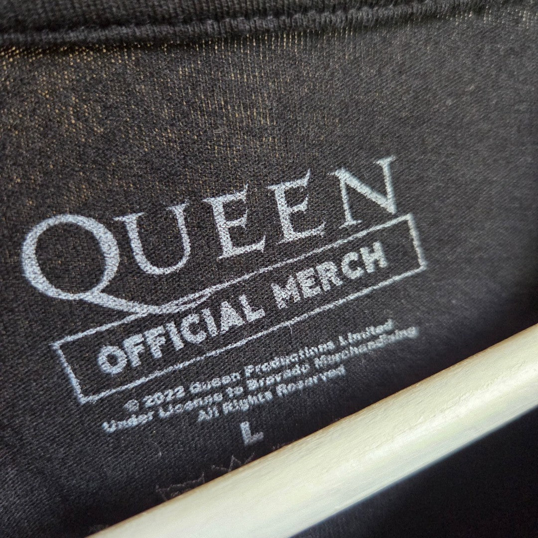 Close-up of a black Upcycled Breastfeeding & Pumping Queen Band t-shirt (size L), featuring the QUEEN official merch logo in white, plus copyright and licensing details. Ideal for fans wanting comfortable nursing wear.
