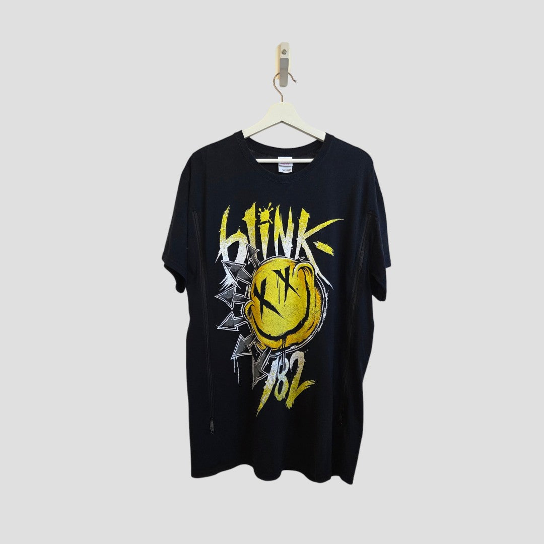 The Gildan Upcycled Breastfeeding & Pumping Blink 182 Yellow Smile Band T-shirt (L, 100250) features a large yellow smiley face and graffiti-style text on black, designed as affordable nursing wear and shown hanging against a light gray background.