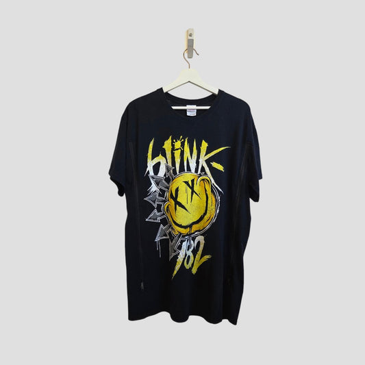 The Gildan Upcycled Breastfeeding & Pumping Blink 182 Yellow Smile Band T-shirt (L, 100250) features a large yellow smiley face and graffiti-style text on black, designed as affordable nursing wear and shown hanging against a light gray background.