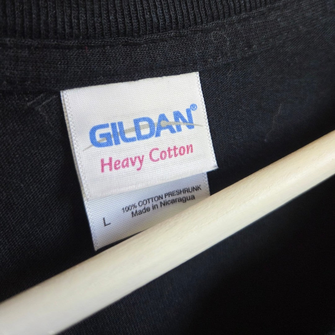 Close-up of a Gildan clothing label on an upcycled "Blink 182 Yellow Smile" nursing & pumping band t-shirt (size L, 100% preshrunk cotton, made in Nicaragua), with part of a hanger visible.