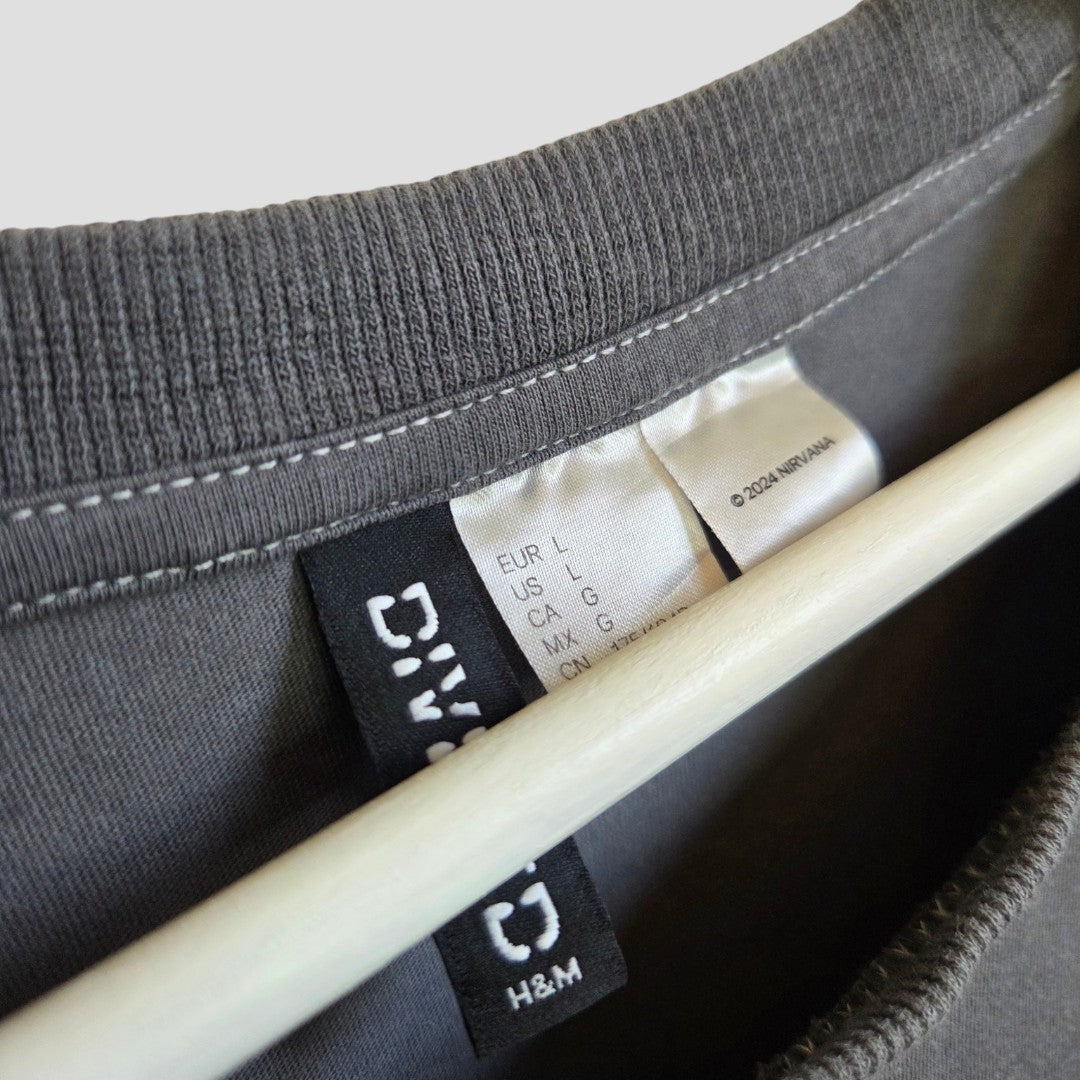 Close-up of a gray H&M Upcycled Breastfeeding & Pumping Nirvana Guitar Band t-shirt (L, 100371) on a hanger, showing the neck seam and tags—an affordable nursing option designed for everyday comfort.