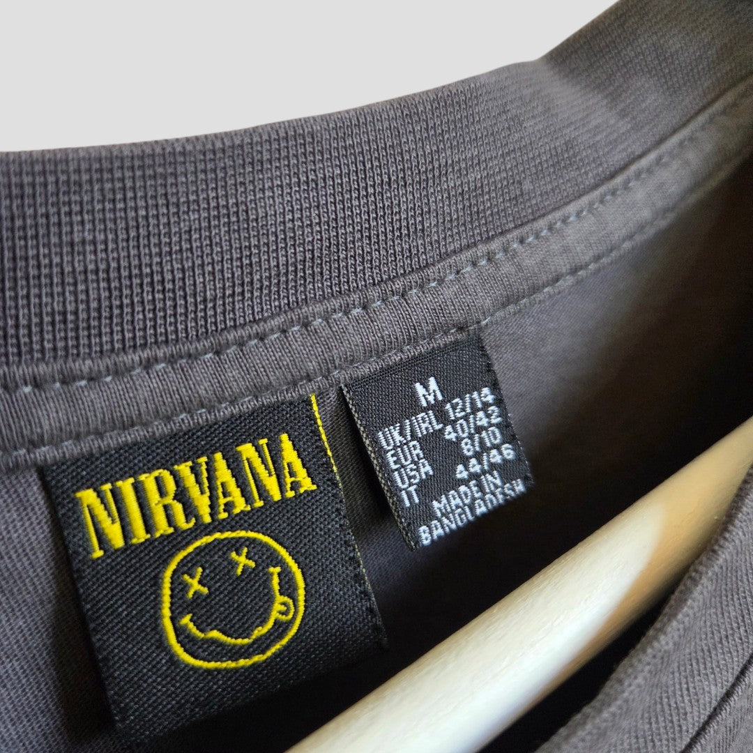 Close-up of a black Primark tag inside an upcycled Nirvana Yellow Smile Band nursing & pumping t-shirt (M UK12/14), with logo and size info. The eco-friendly shirt hangs on a wooden hanger.