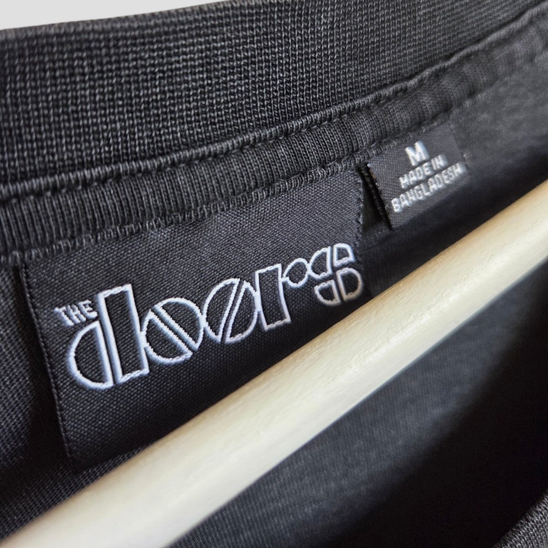 Close-up of a Primark Upcycled Breastfeeding & Pumping Grey/Pink The Doors Band t-shirt (M, UK12/14) with embroidered logo and "Made in Bangladesh" label. Stylish and comfortable nursingwear, shown on a wooden hanger.