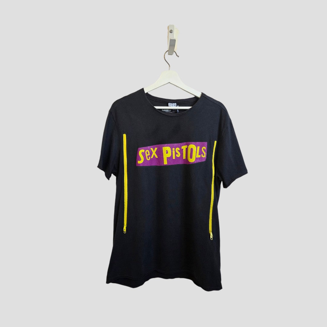 The Amplified Upcycled Breastfeeding & Pumping Grey Sex Pistols Band T-shirt (L) features a bold logo and two vertical yellow zippers from shoulder to side—an edgy, functional piece of nursing wear with punk style.