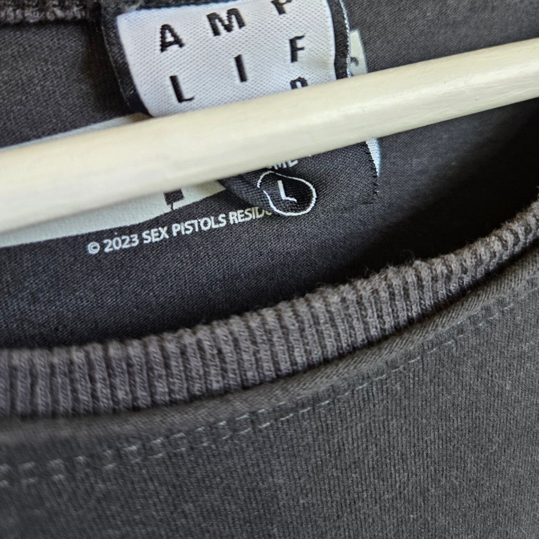 Close-up of an eco-friendly Amplified Upcycled Breastfeeding & Pumping Grey Sex Pistols Band t-shirt (L, 100331) on a hanger, showing the collar with “© 2023 SEX PISTOLS RESID.” tag—ideal for conscious fashion lovers.