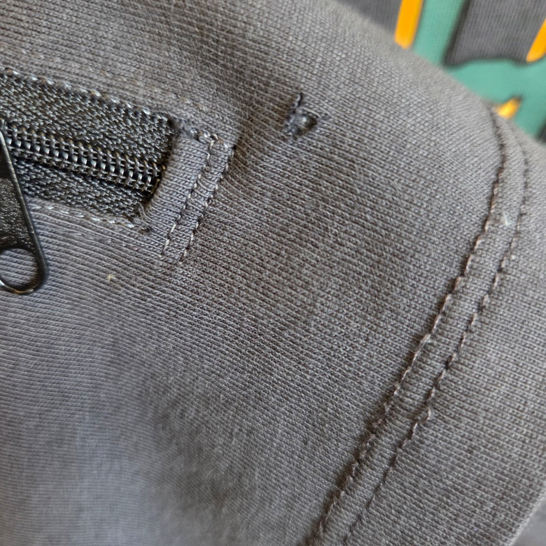 Close-up of black fabric with visible stitching, a small zipper pocket, and a safety pin near the seam—perfect details on this eco-friendly Primark Upcycled Nursing & Pumping Grey Tupac Band t-shirt (L, UK14/16).