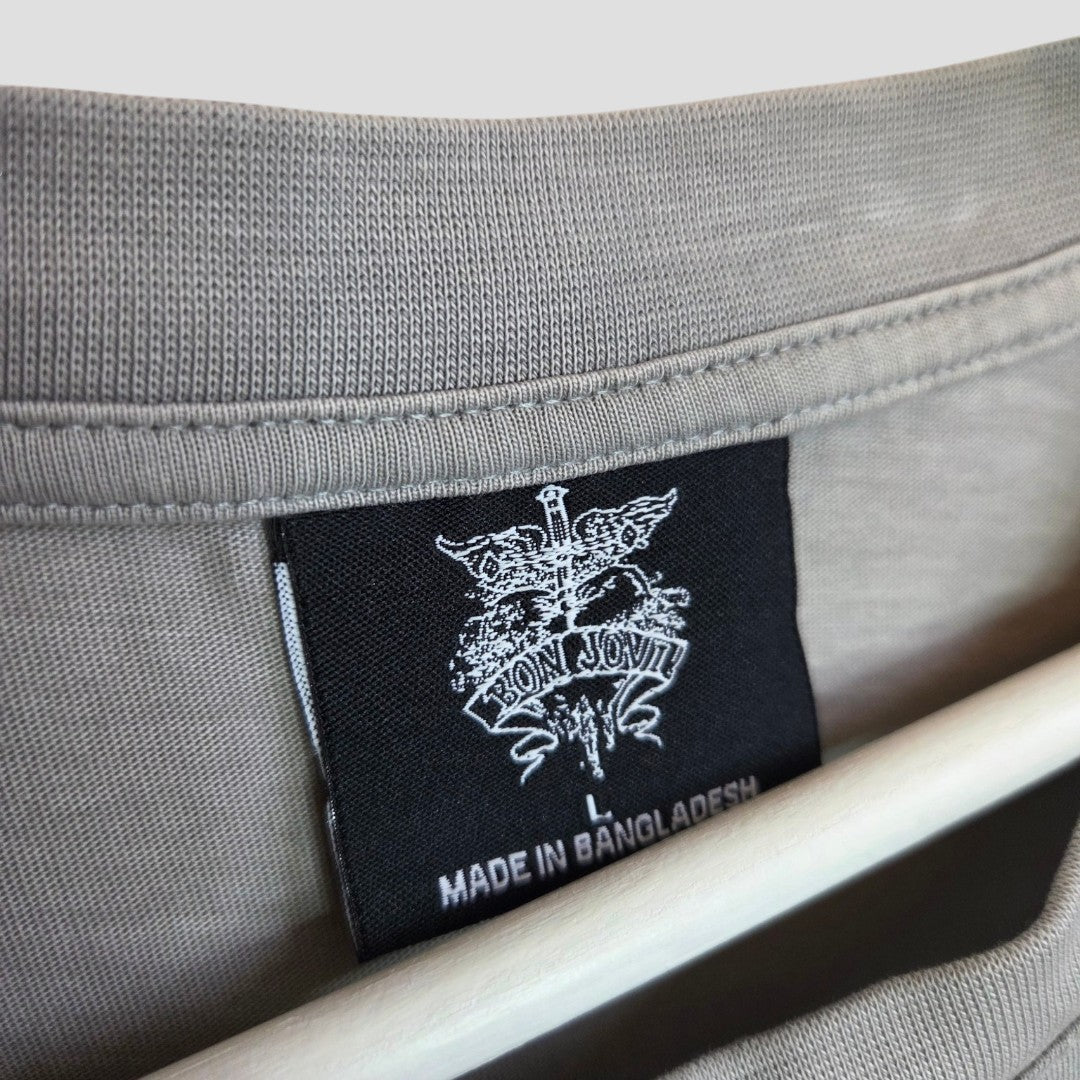 Close-up of a grey Upcycled Breastfeeding & Pumping Bon Jovi Band t-shirt (L) by Primark, made from 100% cotton, featuring a black label with the Bon Jovi logo and "BON JOVI" and "MADE IN BANGLADESH" in white text on the collar.