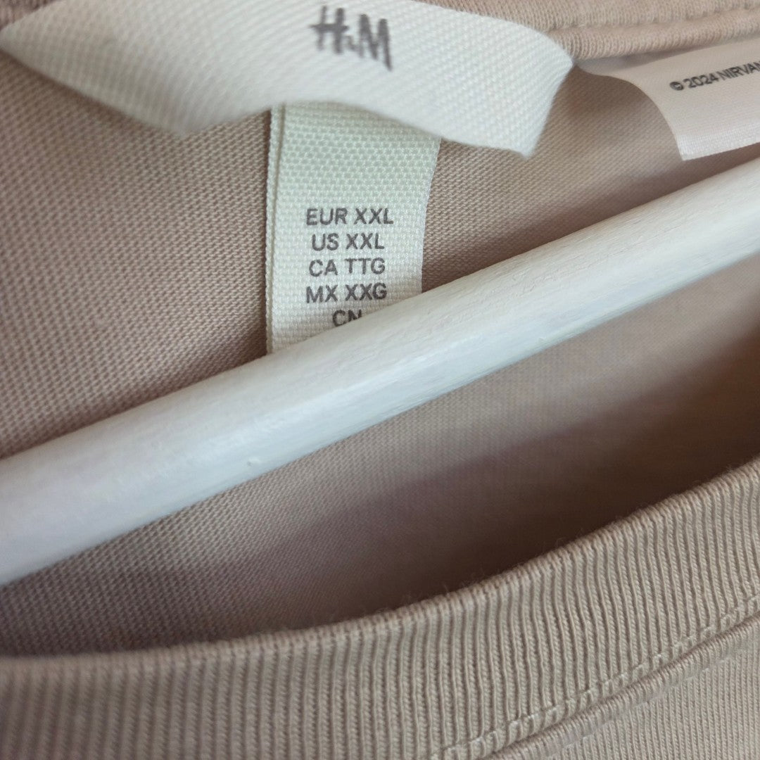 A close-up of the H&M Upcycled Breastfeeding & Pumping Beige Nirvana Smile Band t-shirt (XXL) on a hanger, showing size labels—ideal as affordable maternity or nursing wear for comfort and convenience.