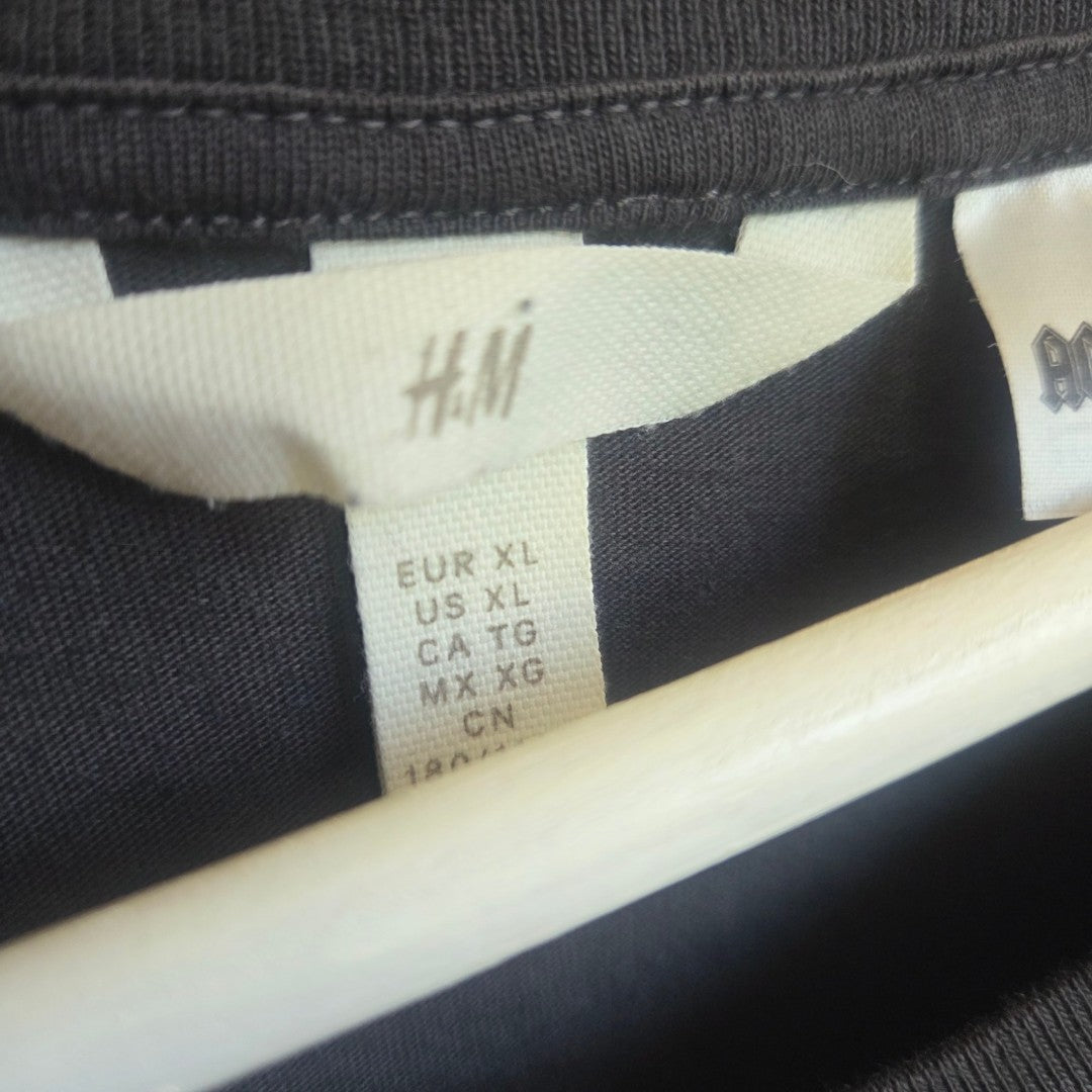Close-up of an H&M label on the Upcycled Breastfeeding & Pumping AC/DC World Tour Band t-shirt XL (100432), showing sizes: EUR XL, US XL, CA TG, MX XG, CN. The black garment is affordable nursing wear with the label at the neckline.