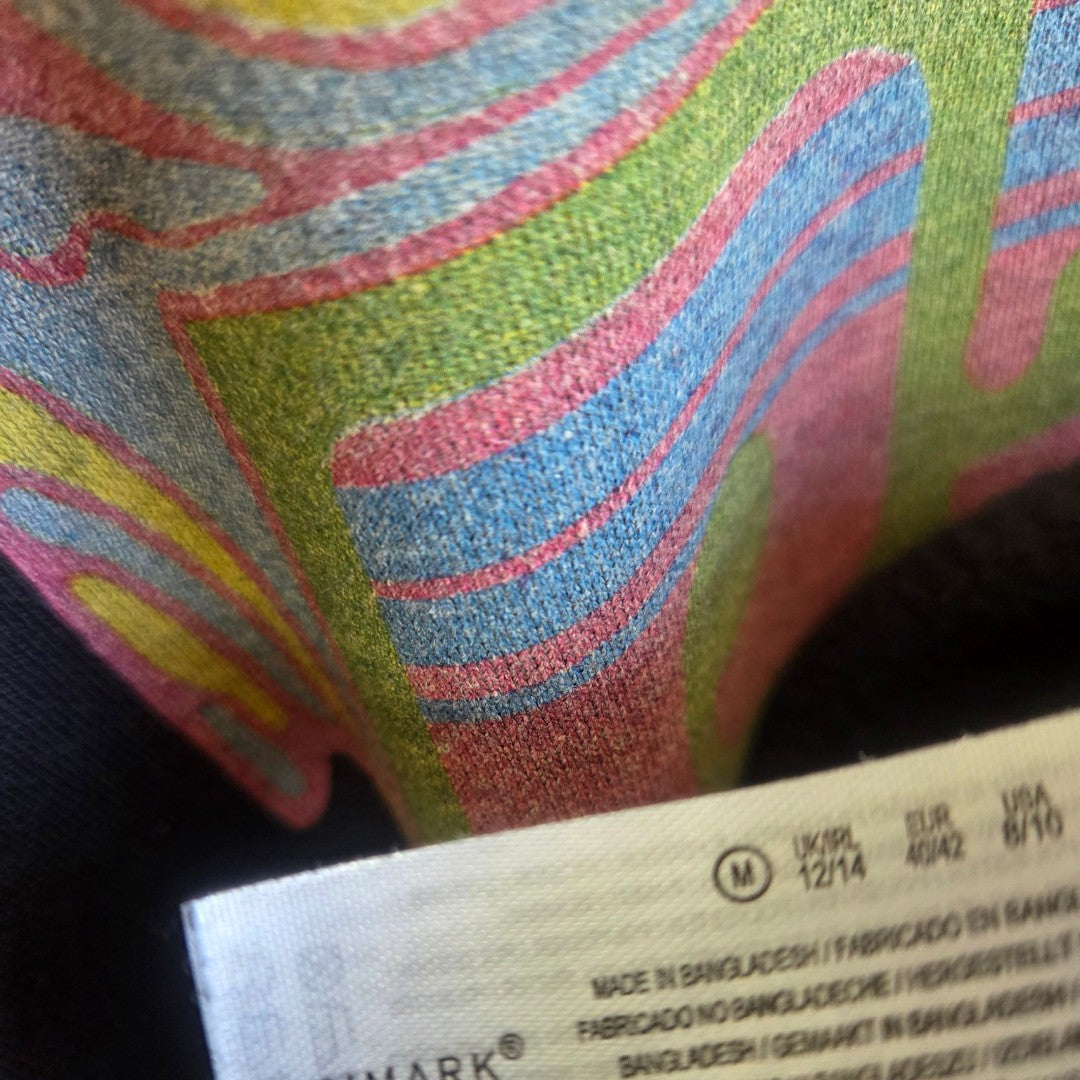 Close-up of a colorful, textured Upcycled Breastfeeding & Pumping Black Pink Floyd Band Sweatshirt by Primark (M/UK12/14). Features visible white label with size and manufacturing details—an eye-catching, affordable nursing piece.
