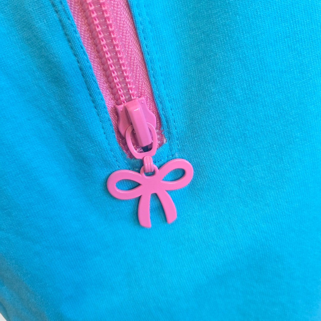 A close-up of a pink zipper with a bow pull on blue fabric—featured on the Primark Upcycled Breastfeeding & Pumping Turquoise/Pink Girl Bow t-shirt M (UK12/14).