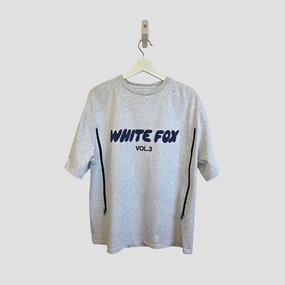 An eco-friendly White Fox Upcycled Breastfeeding/Pumping Grey/Blue T-shirt (L) featuring WHITE FOX VOL.3 in bold navy on the front, shown on a white hanger against a plain light background.