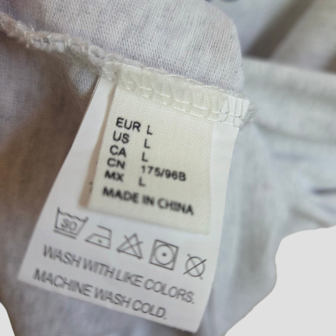 A close-up of the White Fox Upcycled Breastfeeding & Pumping Grey/Blue t-shirt size L label shows regional sizing, Made in China, and care symbols with instructions: Wash with like colors. Machine wash cold.