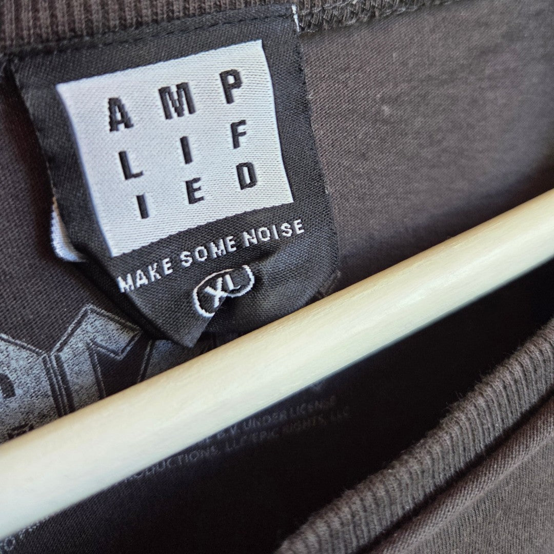 A close-up of the black label on an Amplified Upcycled Breastfeeding & Pumping Grey AC/DC Highway Band t-shirt XL (100485), reading "AMPLIFIED" and "MAKE SOME NOISE," is shown on a wooden hanger.