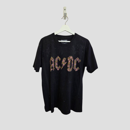 An upcycled black AC/DC band t-shirt (size L) for breastfeeding and pumping, featuring colorful floral logo letters, hangs on a white hanger against a gray background.