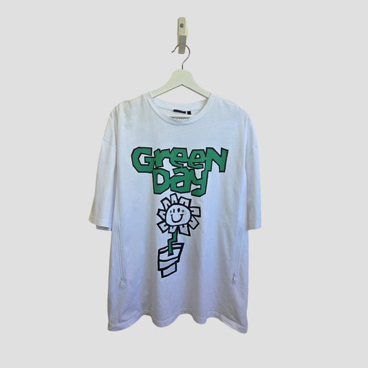 An ASOS Upcycled Breastfeeding & Pumping White Green Day Band T-shirt (XL, 100493) hangs on a hanger, featuring bold green "Green Day" text and a black smiling flower-in-pot graphic against a light gray background.