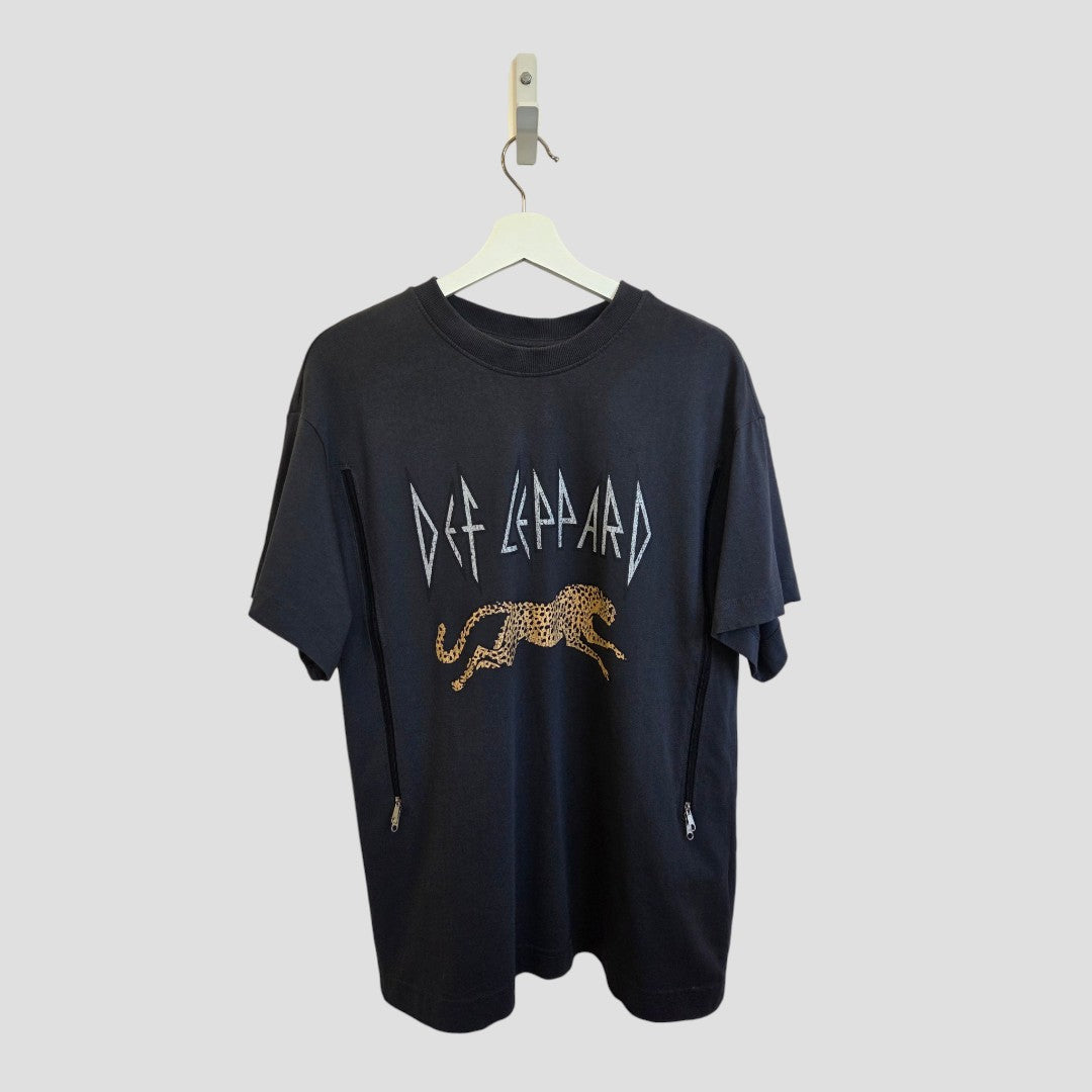 An upcycled H&M Def Leppard band T-shirt (nursing & pumping, size M) with a leopard print and stylized white band lettering hangs on a white hanger against a plain gray background.